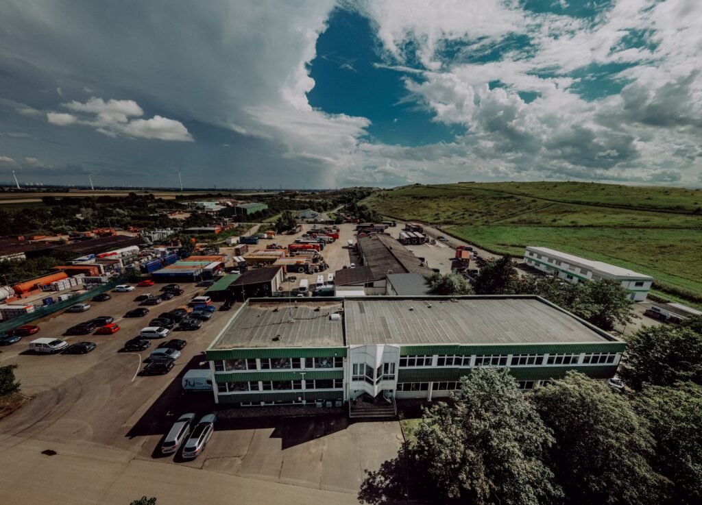 Der Firmenstandort der WILLERSINN Gruppe in Heßheim aus der Vogelperspektive zeigt das Hauptgebäude und Nebengebäude, PKW und LKW. Die Deponie sowie die Nachbarschaft im Hintergrund.